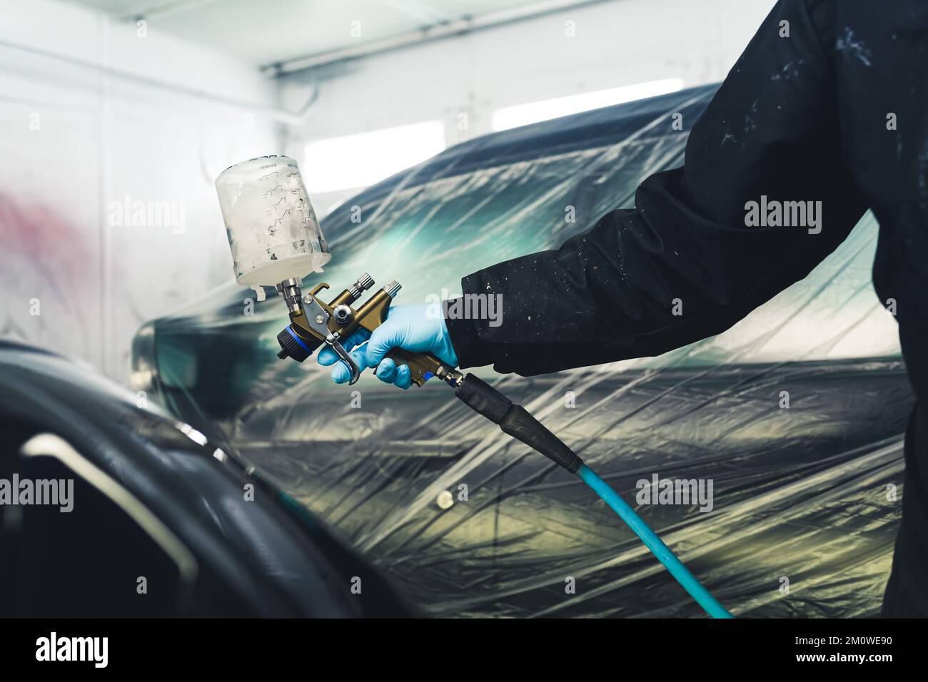 Use of paint spray gun. Indoor shot of an arm of a person in protective coveralls and gloves holding paint spray gun in a paint spray booth. High quality photo Stock Photo