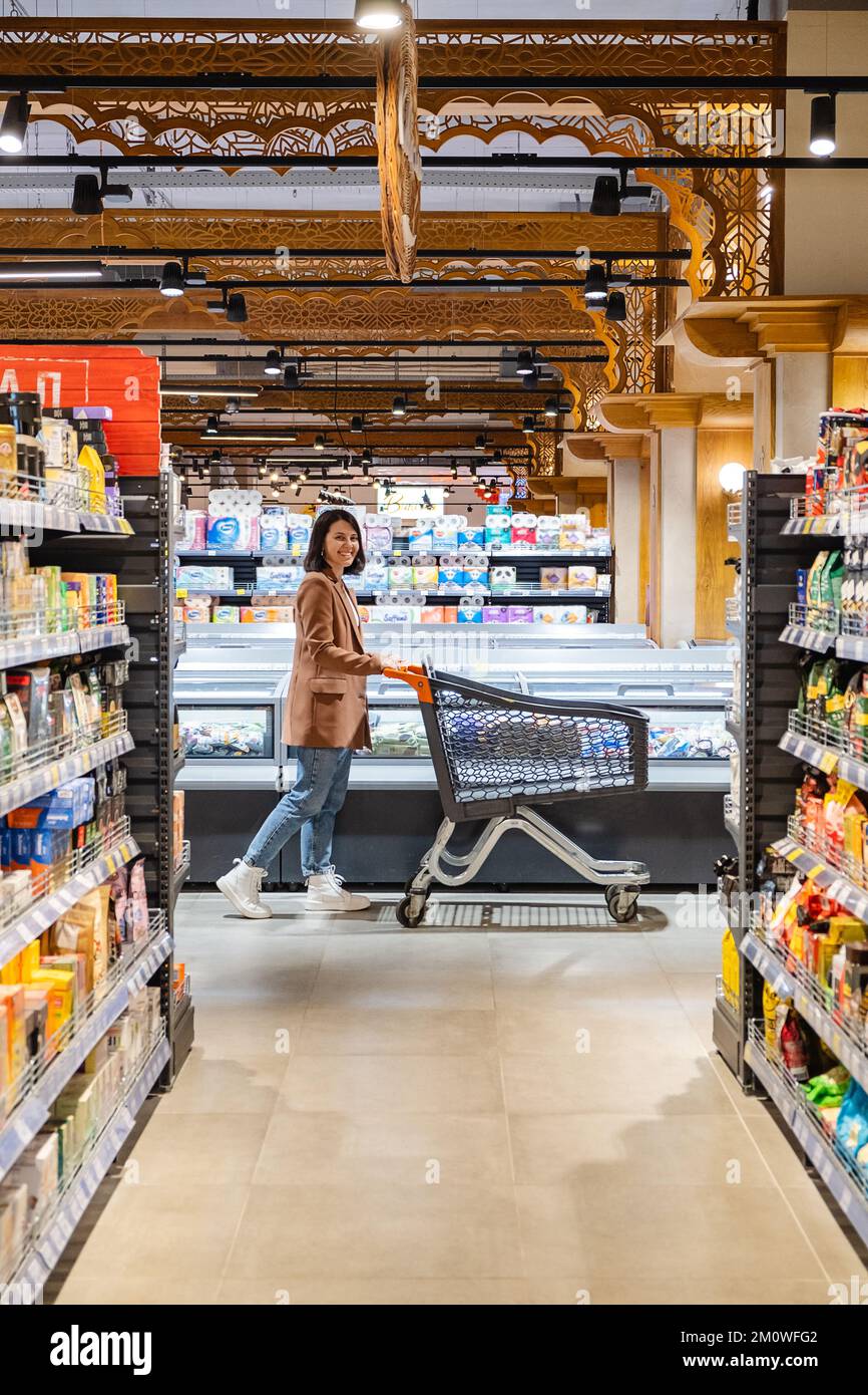 a woman with a cart walks between rows of shelves in a grocery store ...