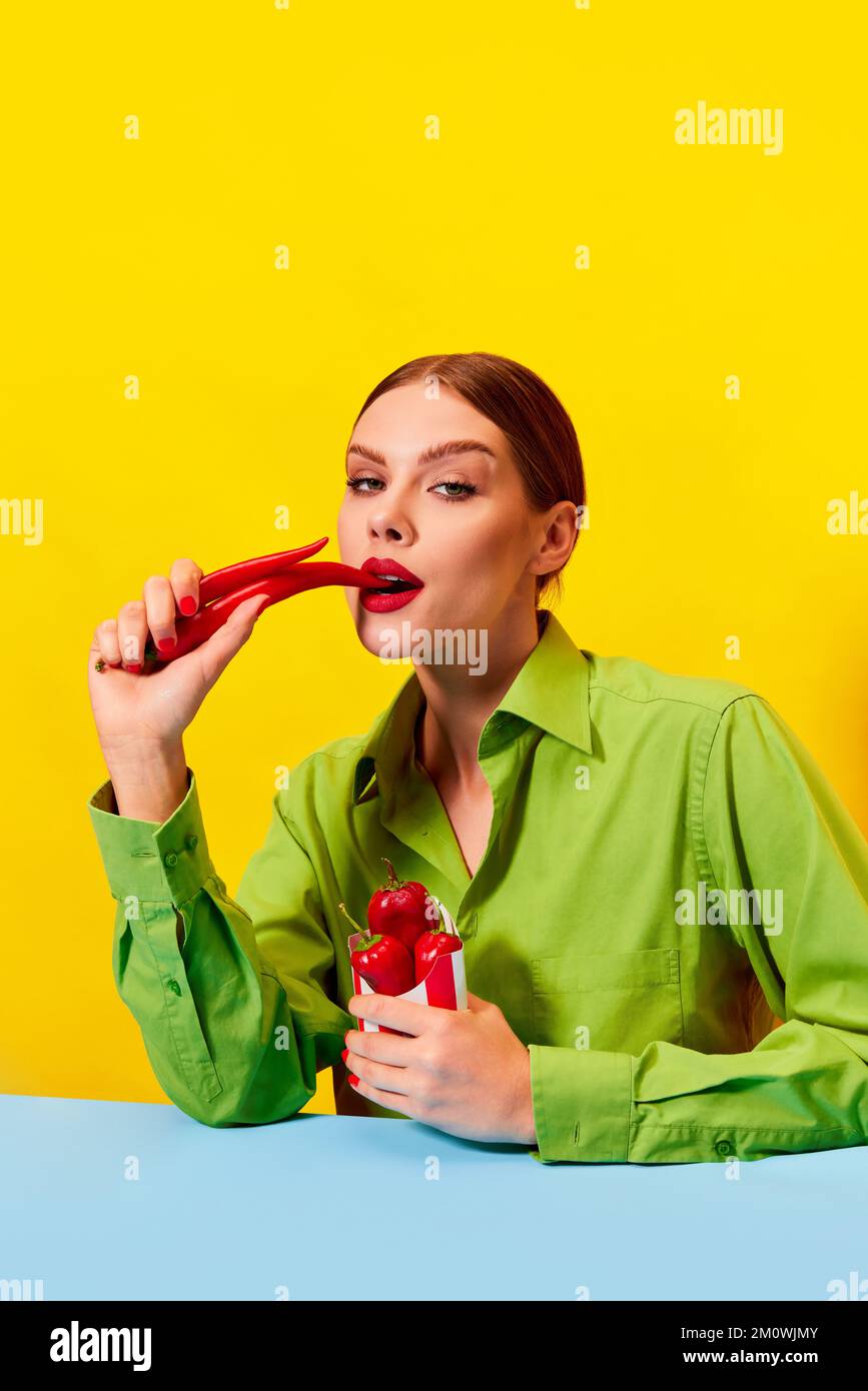 Beuatiful young woman in vintage green jacket eating red chilli pepper