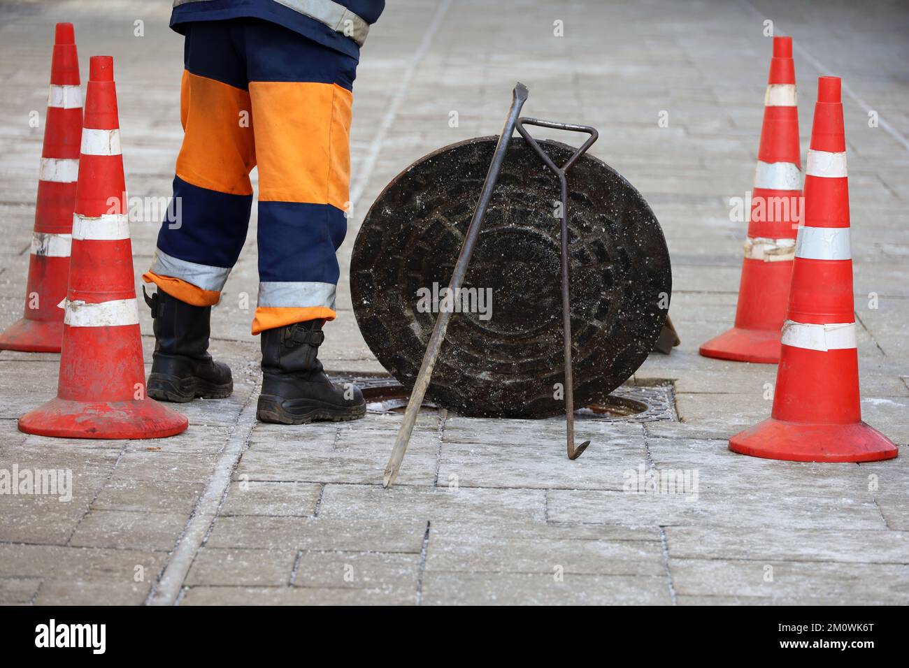 Worker standing over the open sewer hatch on winter street. Concept of repair of sewage, underground utilities, cable laying Stock Photo