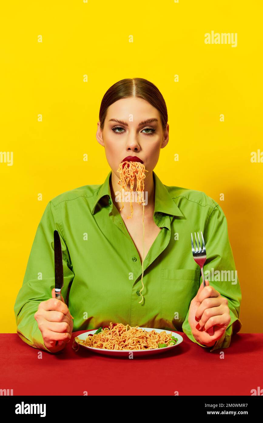 Young girl eating spaghetti, noodles sticking out of the mouth over yellow background. Dinner