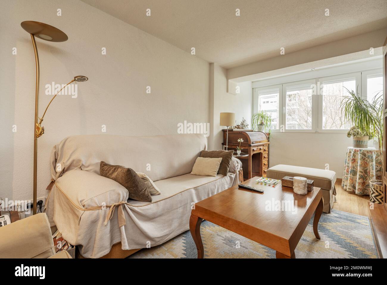 Living room with sofa covered with protective cloth, wooden coffee table and gazebo with white aluminum windows Stock Photo