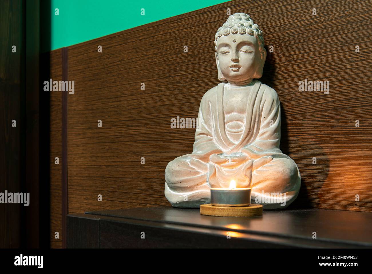 A white stone figure of Buddha on a dark wooden sideboard Stock Photo