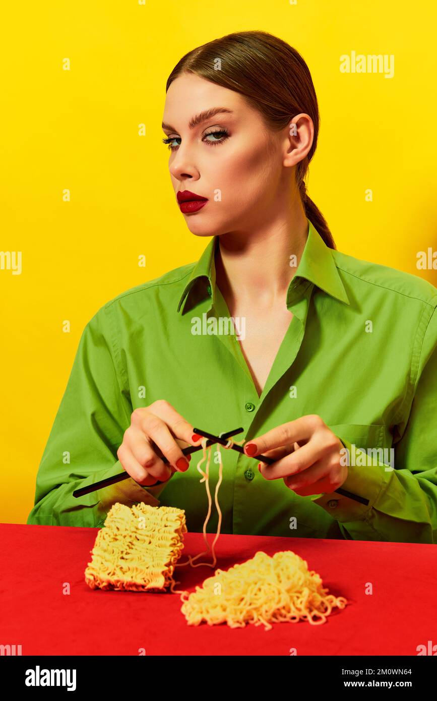 Woman with emotionless face knitting instant noodles on blue table on ...