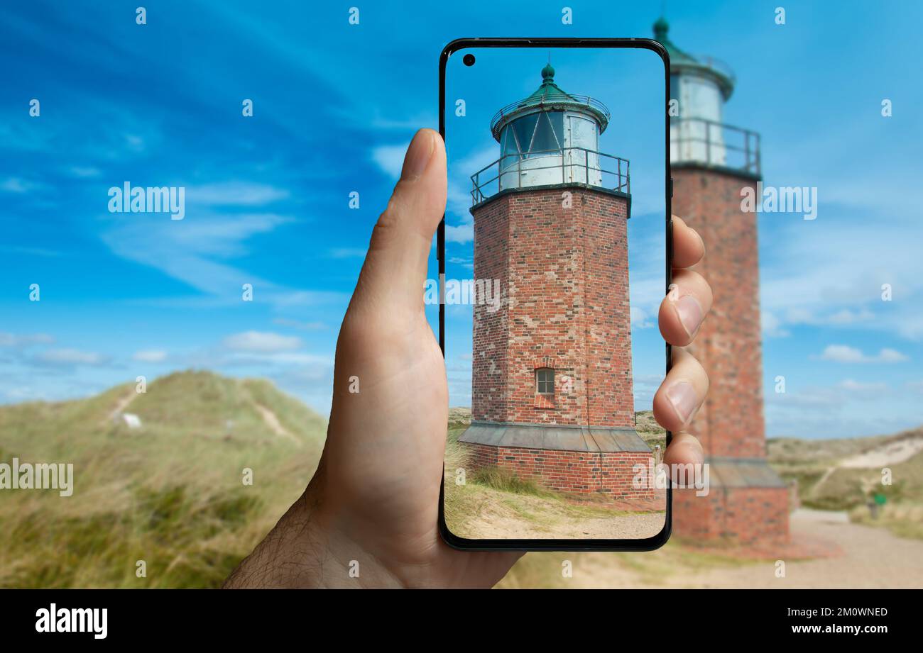Tourist taking a picture with a mobile phone of the lighthouse 'rotes kliff' on the Island Sylt, Germany. Stock Photo