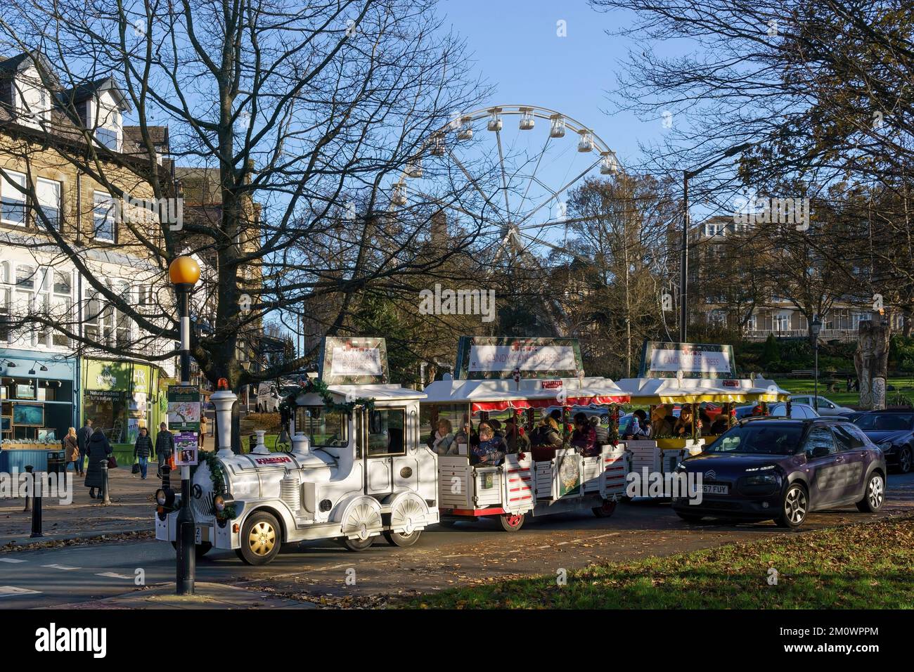Christmas shoppers on the Candy Cane Express Road Train ride along a street with the Ferris wheel as a backdrop, in Harrogate,Yorkshire, England, UK. Stock Photo