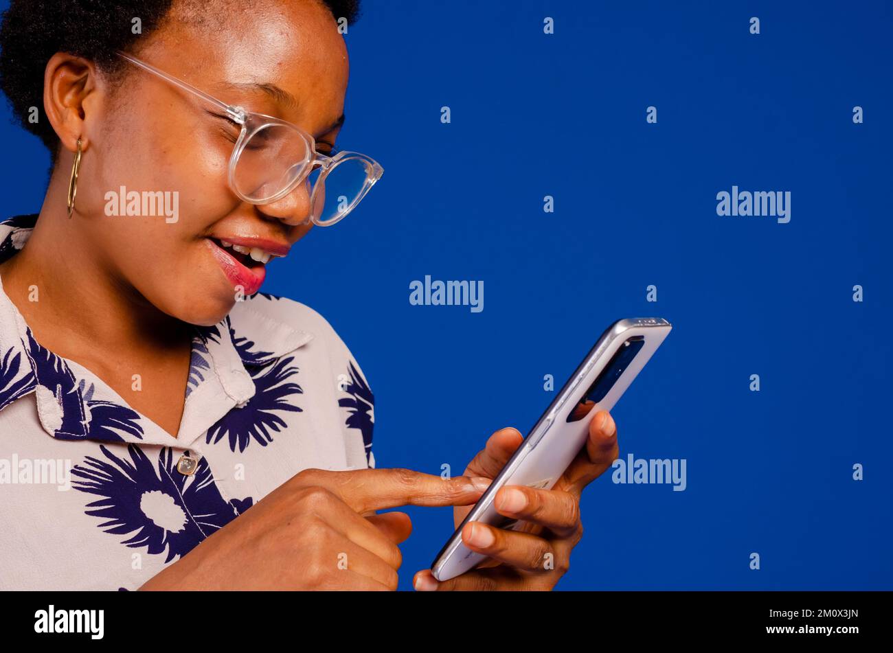 A closeup of a black lady scrolling her phone isolated on a blue background. Stock Photo