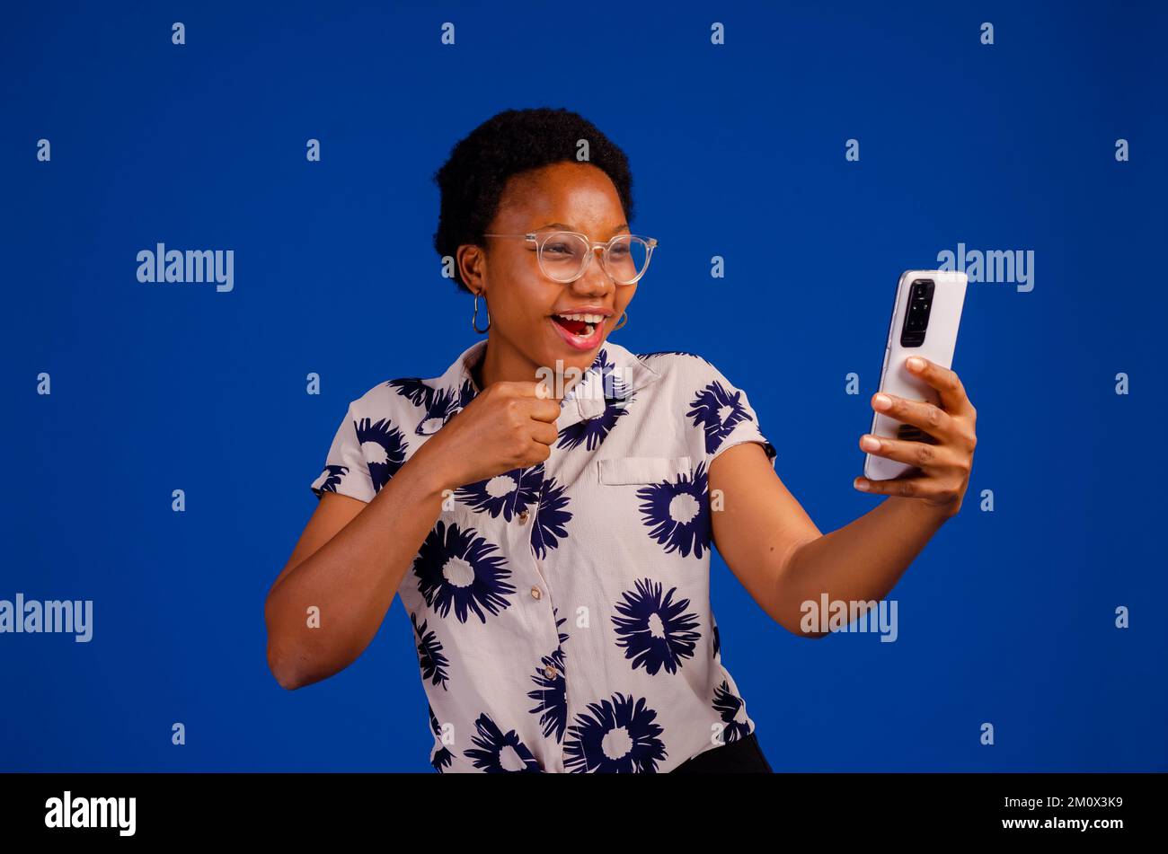 An overexcited black lady with her phone isolated on a blue background. Stock Photo