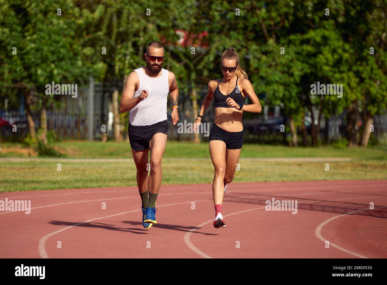 Young family promoting healthy lifestyle. Woman and man run stadium. Coach and sportsman motion run training before race. Couple runners training outd Stock Photo