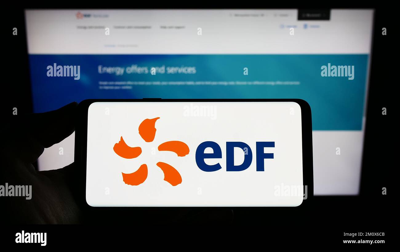 Person holding mobile phone with logo of energy company Electricite de France S.A. (EDF) on screen in front of web page. Focus on phone display. Stock Photo