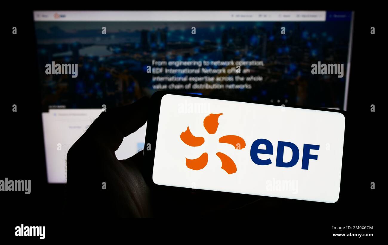 Person holding cellphone with logo of energy company Electricite de France S.A. (EDF) on screen in front of webpage. Focus on phone display. Stock Photo