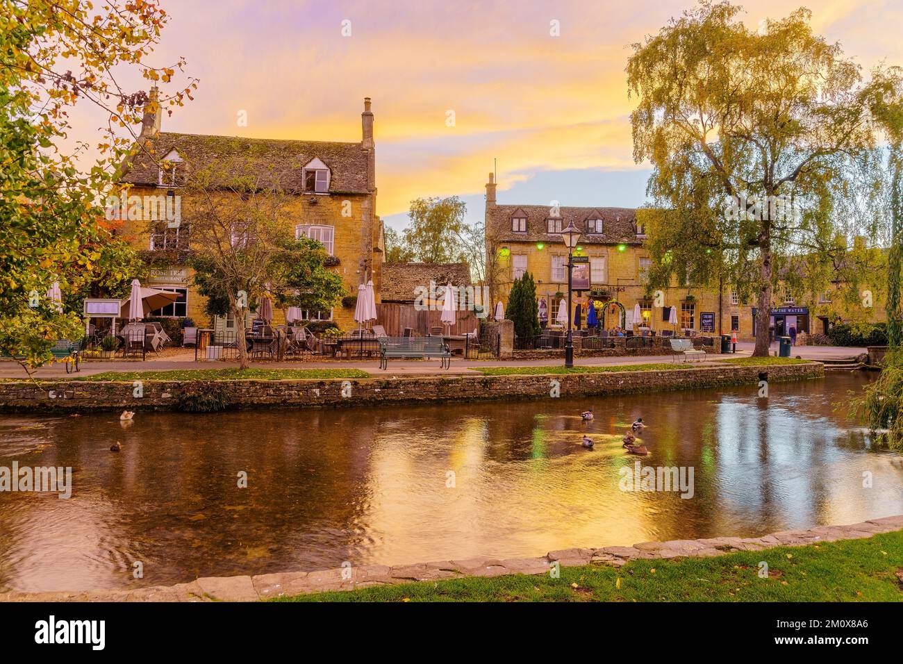 Bourton-on-the-Water, UK - October 17, 2022: Sunset scene of typical houses, the river Windrush, locals and visitors, in the village Bourton-on-the-Wa Stock Photo
