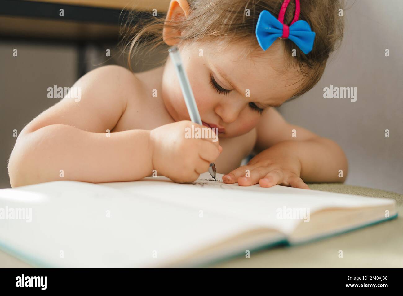 Baby girl having fun with pencil and drawing on paper at table at home. Creative thinking and artistic concepts. Education concept. Stock Photo