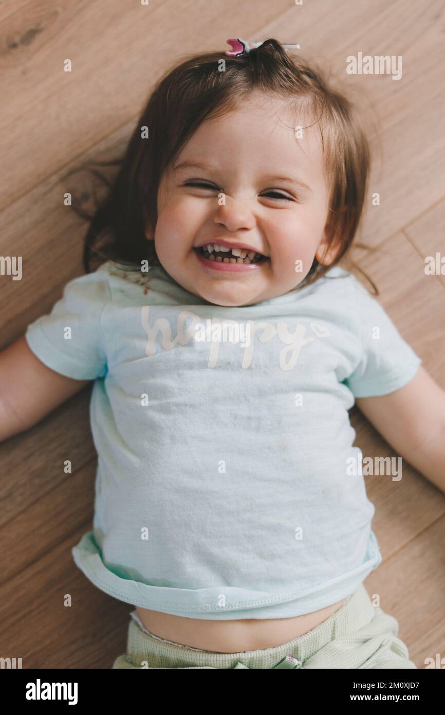 Adorable laugh baby girl lying on her back on the floor of a light home ...