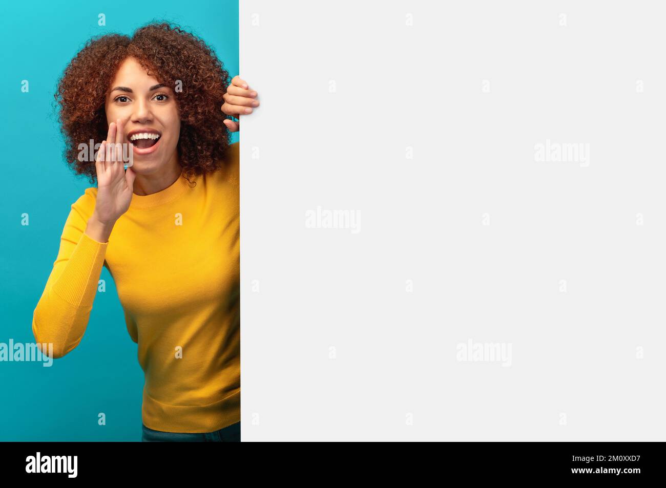 African American woman peeking out from empty white board and holding her hands near her mouth scream Stock Photo