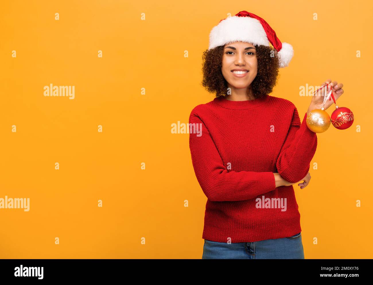African American woman in santa claus hat on orange background, Happy woman holds in hands christmas balls. Xmas concept Stock Photo
