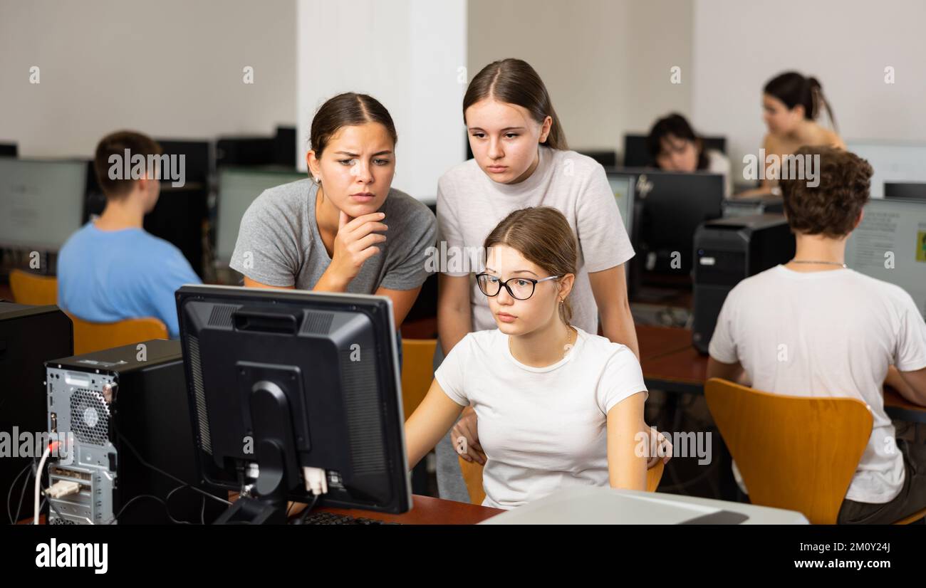 Two smart female teenagers helping to the co-learner while she is using computer in the classrooms Stock Photo
