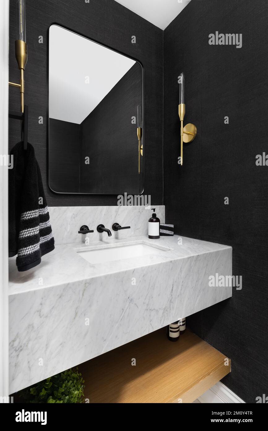 A bathroom with black wallpaper, gold sconces, and a floating marble