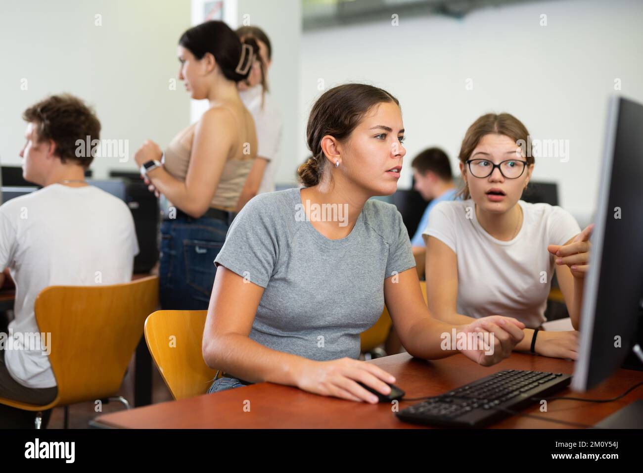 Schoolgirl using computer and teacher helping to him in class room ...