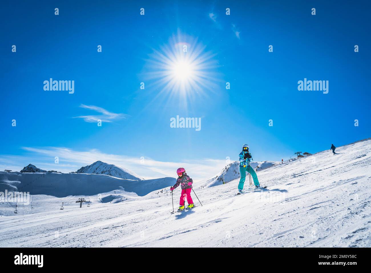 Mother teaching daughter how to ski, skiing down on a ski slope. Sunny