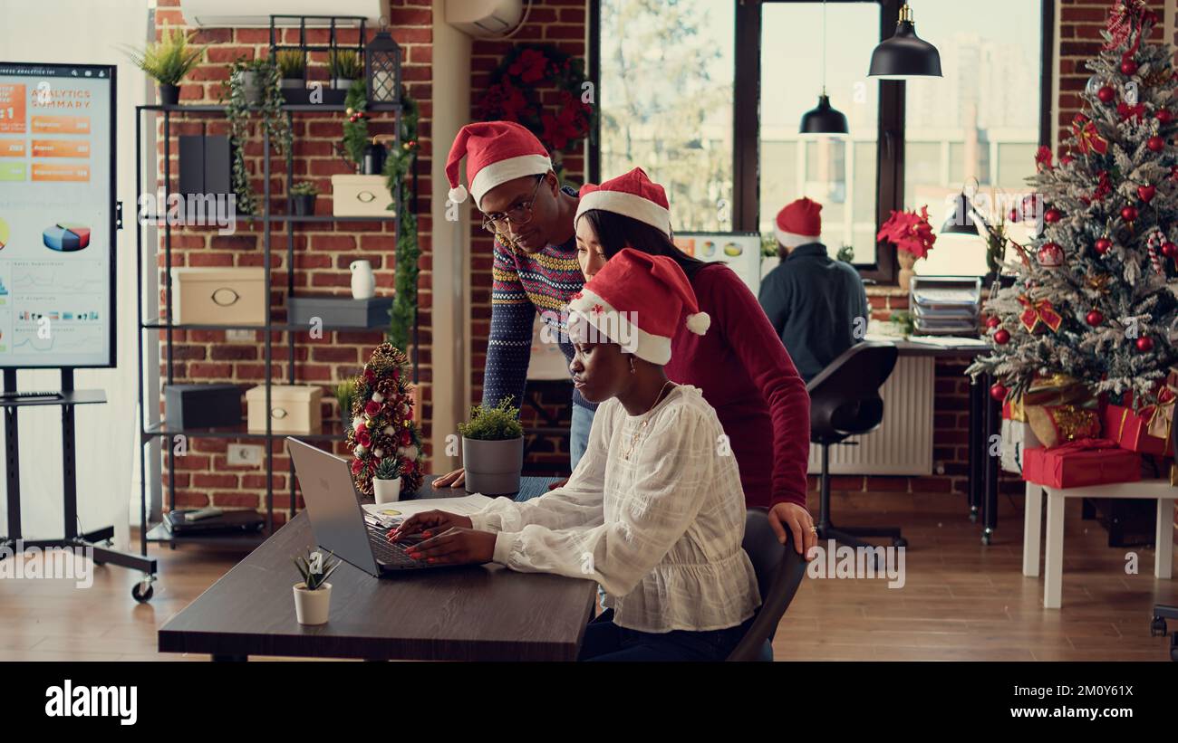 Diverse colleagues brainstorming ideas on laptop, doing teamwork in festive decorated office 