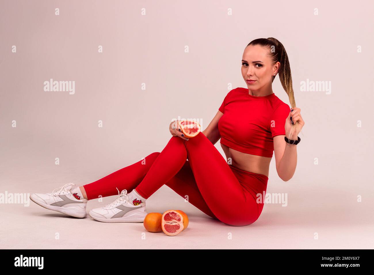 A young woman in a red suit holds a cut grapefruit in her hands Stock Photo