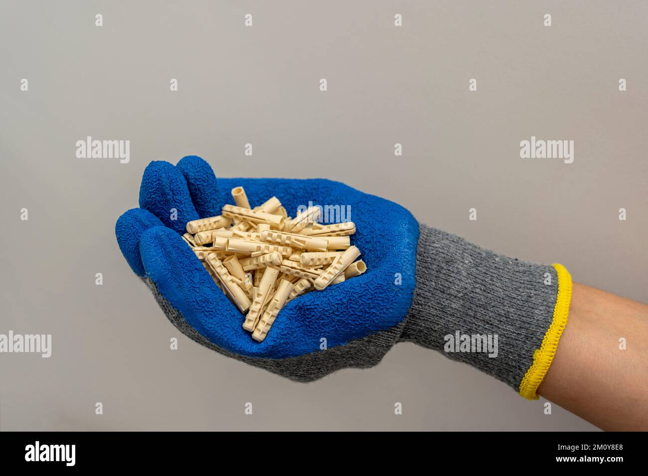 A worker's hand in a protective glove holds a bunch of plastic dowel pins Stock Photo
