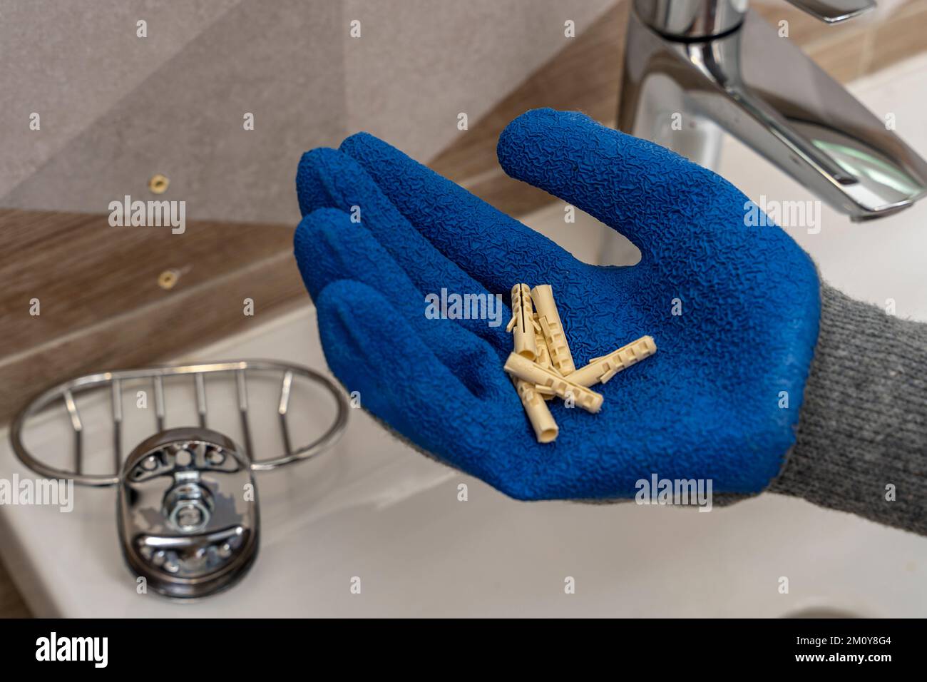 worker's hand in a protective glove holds several plastic dowel pins Stock Photo