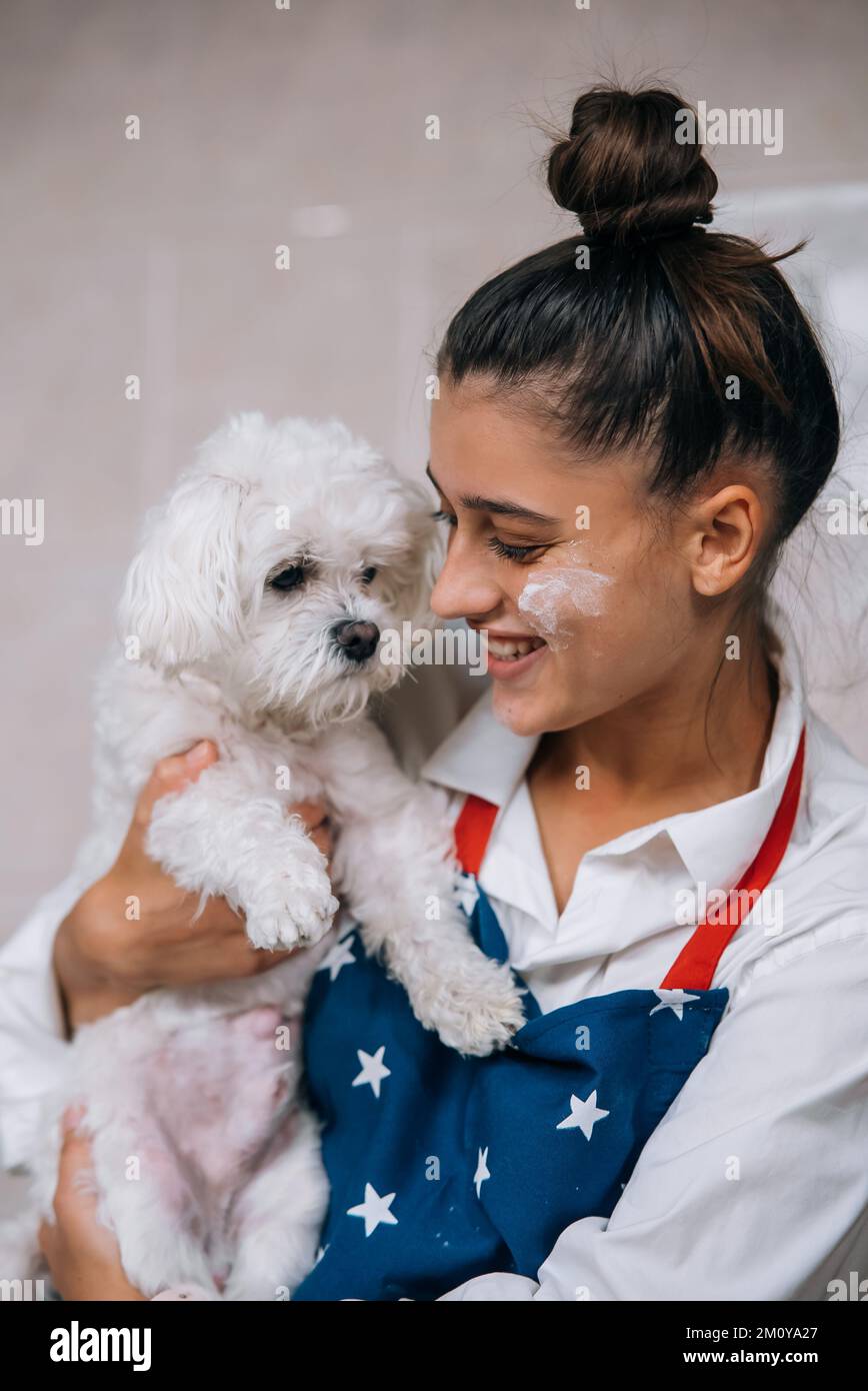 Smiling woman in kitchen holding cute white Maltese dog Stock Photo