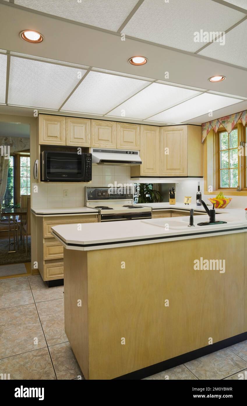 Bleached tan yellowish wooden cabinets in kitchen inside mixed decorated and architectural style home. Stock Photo