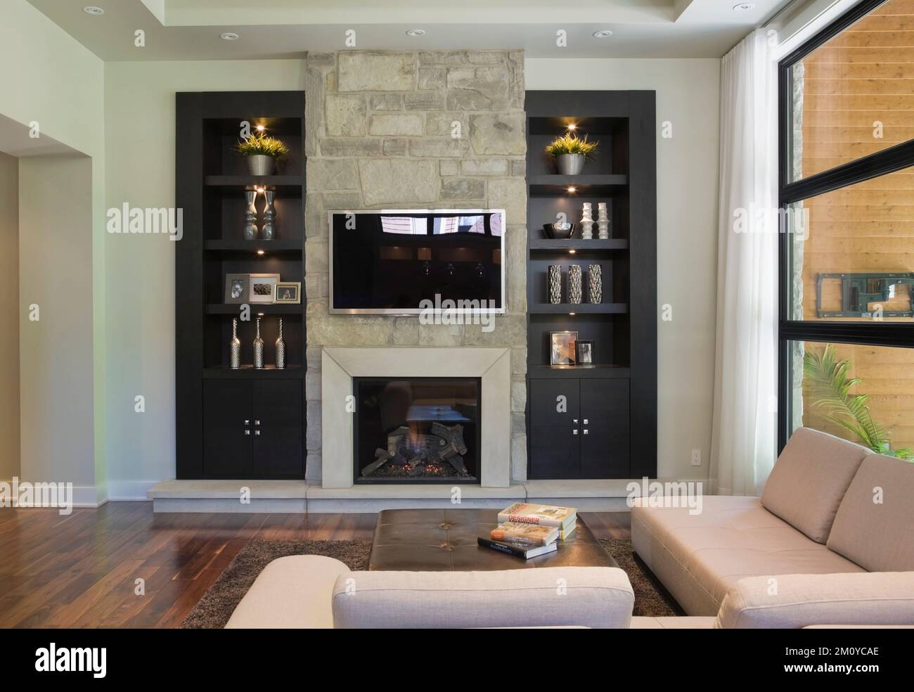 Black wall unit with natural stone fireplace and sectional sofa in living room inside upscale