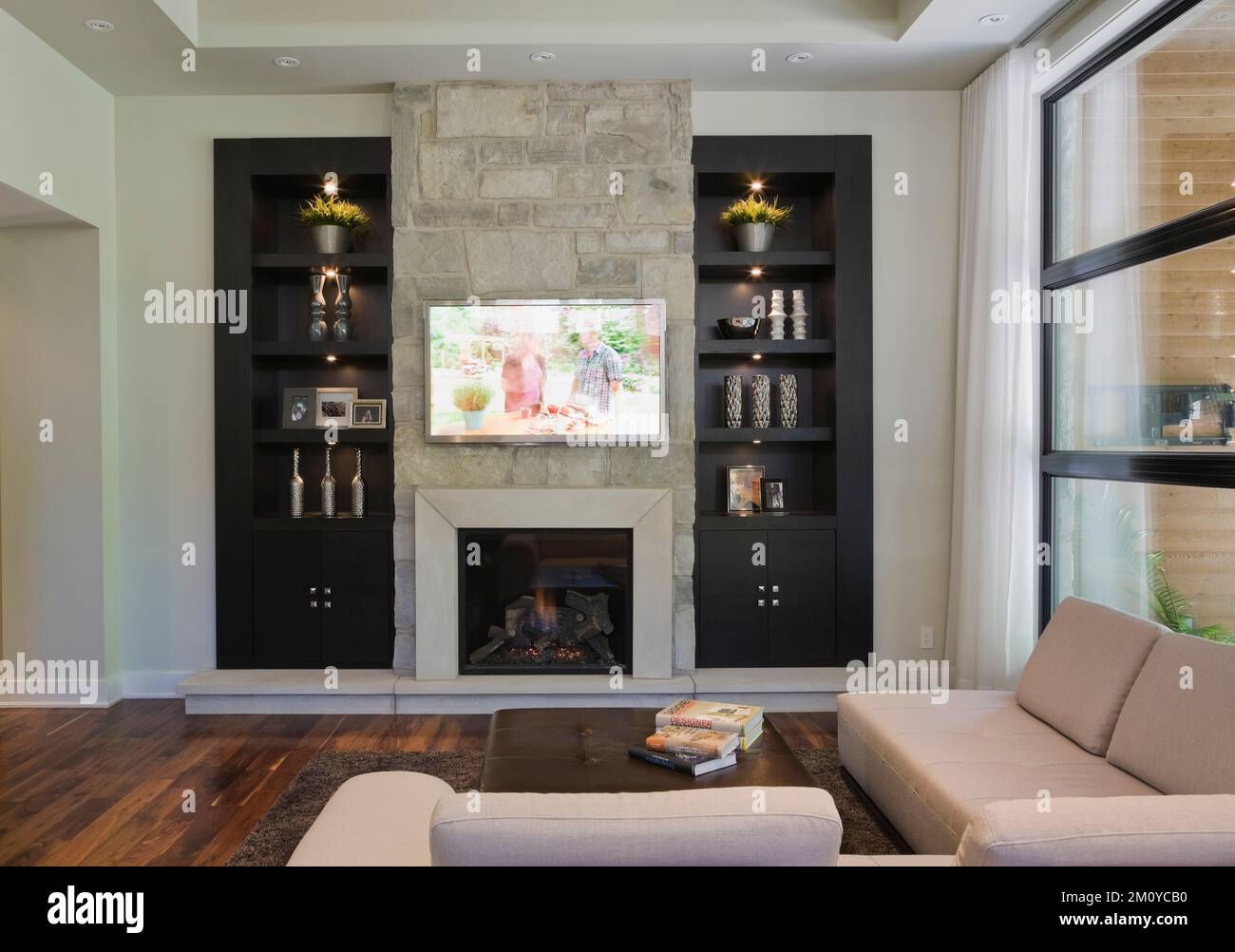 Black wall unit with natural stone fireplace and sectional sofa in living room inside upscale home. Stock Photo