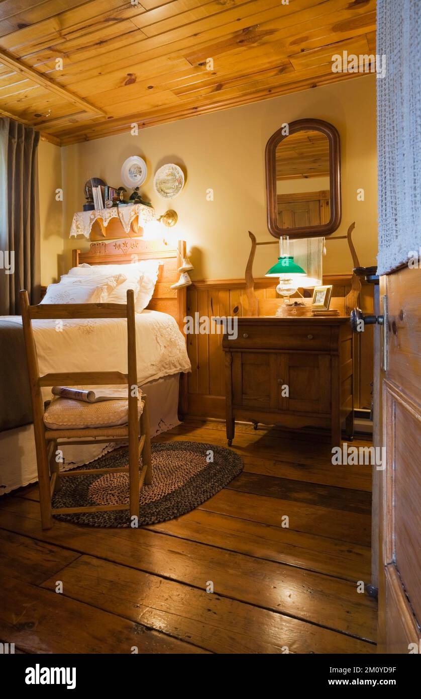 Antique rocking chair next to single bed in guest bedroom inside 1977 built replica of old 1800s Canadiana cottage style log home. Stock Photo