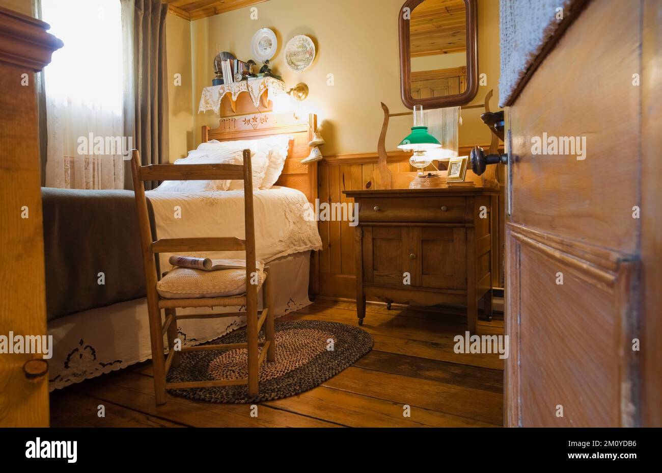 Antique rocking chair next to single bed in guest bedroom inside 1977 built replica of old 1800s Canadiana cottage style log home. Stock Photo