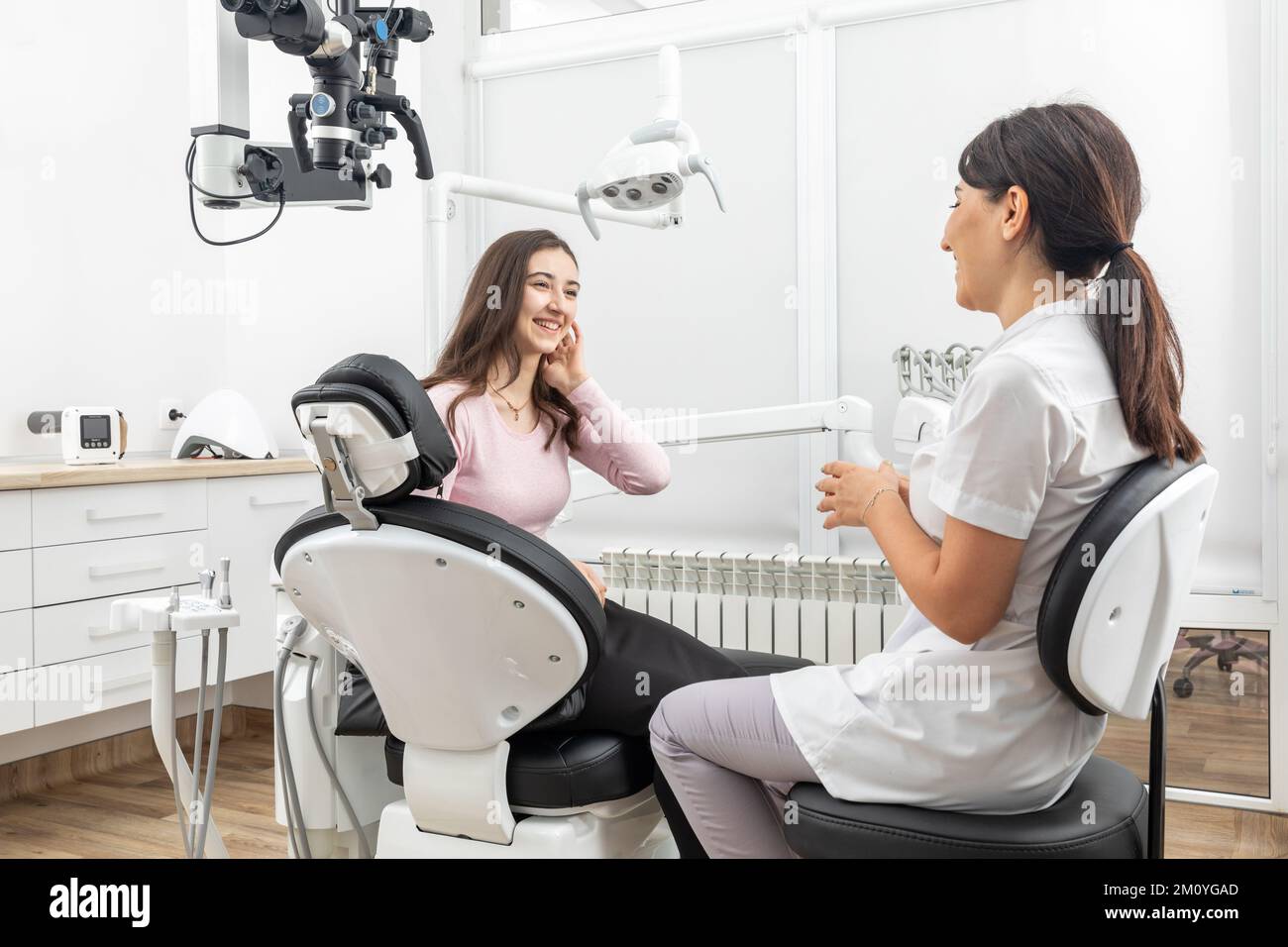 Female dentist talking to a young patient during appointment in modern ...