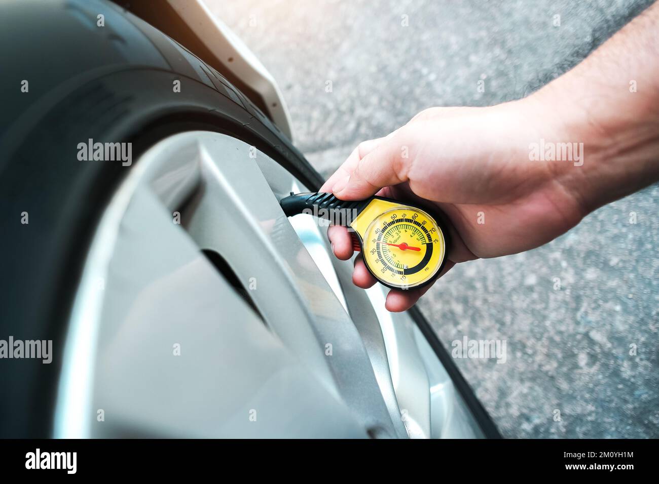 The driver is measuring the tire pressure with a  standard tire pressure gauge, auto maintenance service concept Stock Photo