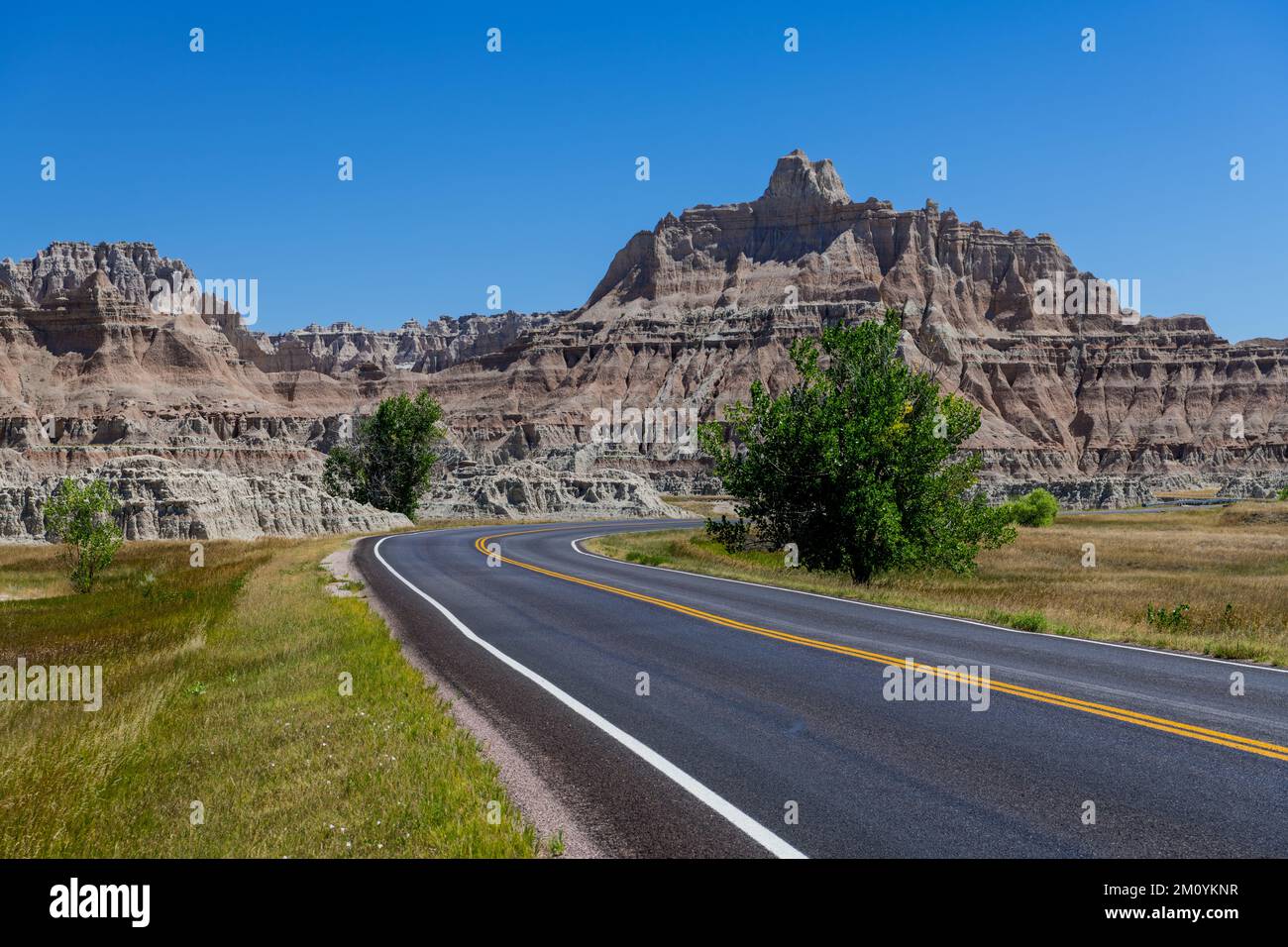 A highway curves through a beautiful landscape of grassy meadow toward a colorful peak in Badlands National Park, South Dakota Stock Photo