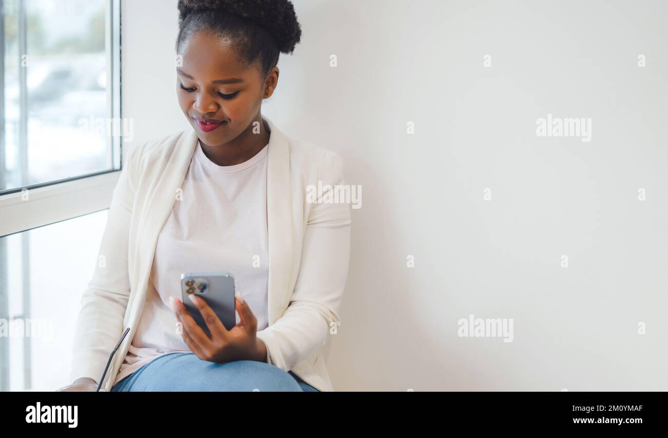 Beautiful happy business african woman with a phone in her hands sitting in a cafe drinking an ice coffee. Girl rest and working in a cafe Stock Photo