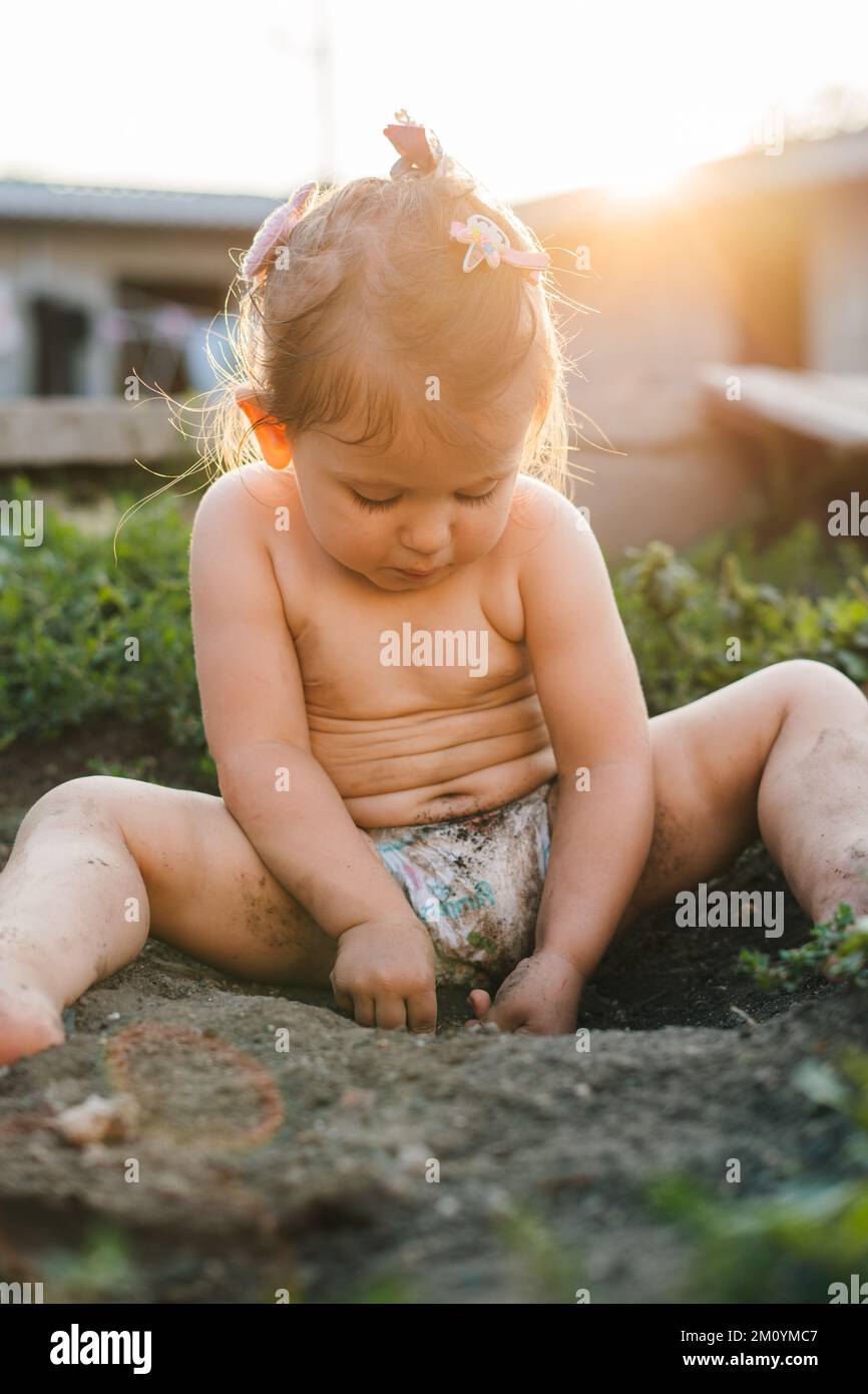 Portrait of adorable baby girl playing in the garden, getting dirty while exploring and learning that is in the garden. Little garden. Nature summer. Stock Photo