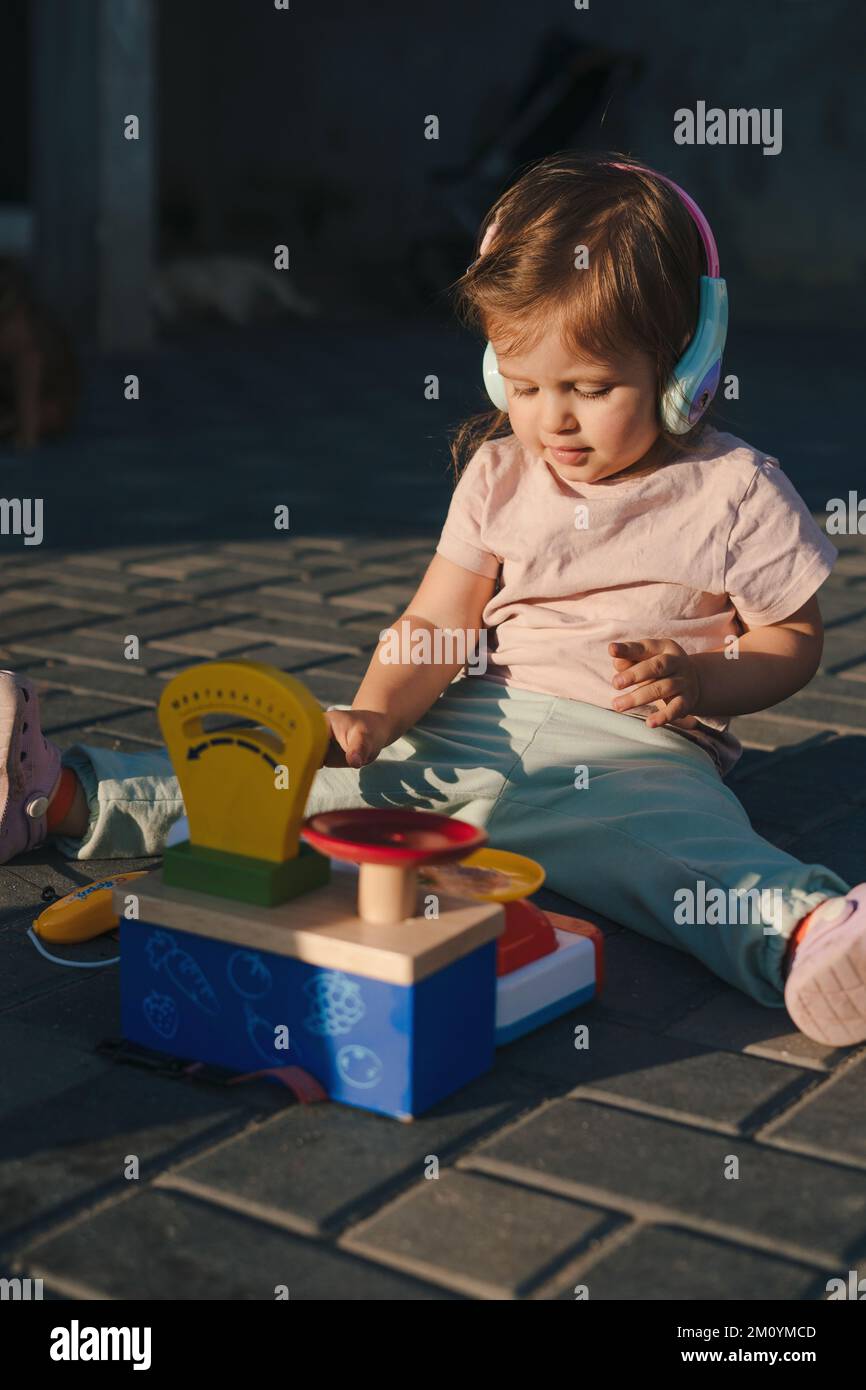 Adorable little baby girl playing with plastic toys outside, imitating saleswoman. Children education concept. Healthy kids summer activity. Stock Photo