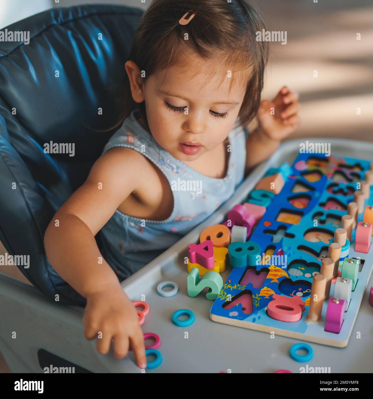 Cute baby girl playing with colorful rainbow toy sitting on highchair