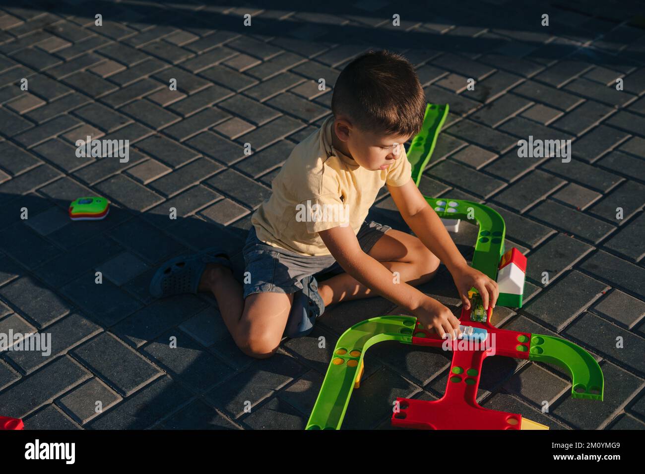 A boy playing outside in the yard of the house at sunset with cars doing competition. Educational toys. Happy family. Family education. Stock Photo