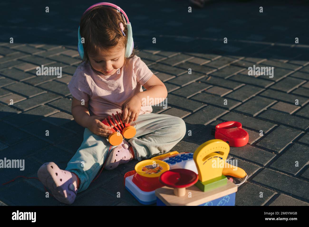 Baby girl sitting in the garden at sunset playing with many toys that develop skills. Nature summer. Educational toys. Happy family. Stock Photo