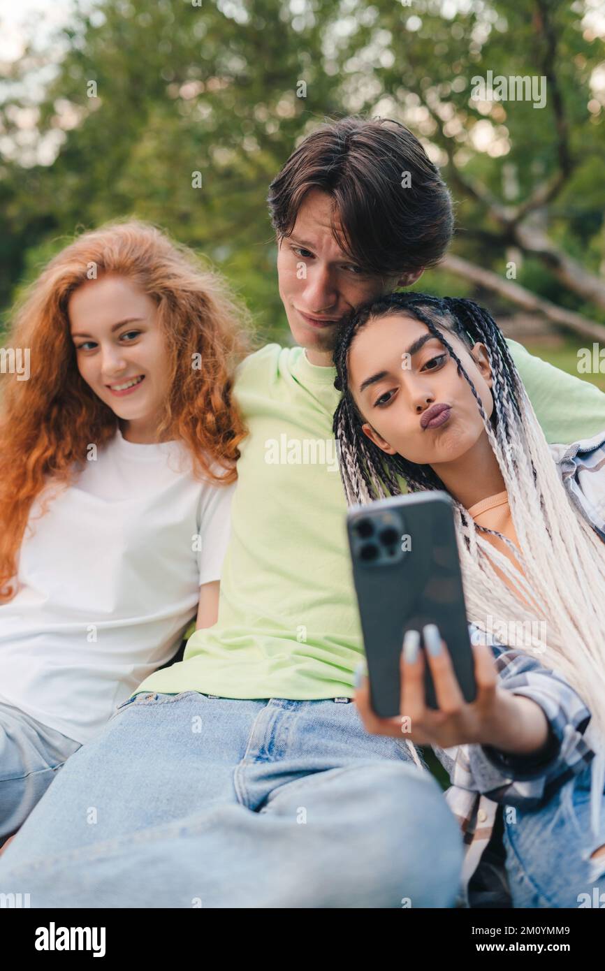 Three friends taking a selfie outdoors on sunny summer day, sitting in the bark. Summer vacation fun. Having fun. Stock Photo