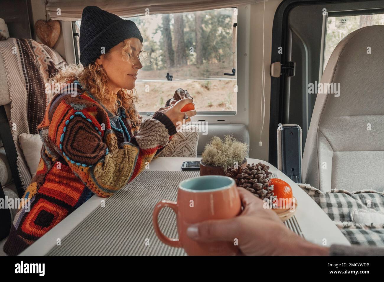 Happy couple enjoy time drinking tea inside a camper van. Nomadic lifestyle tourists people having relax leisure activity inside vehicle motor home. R Stock Photo