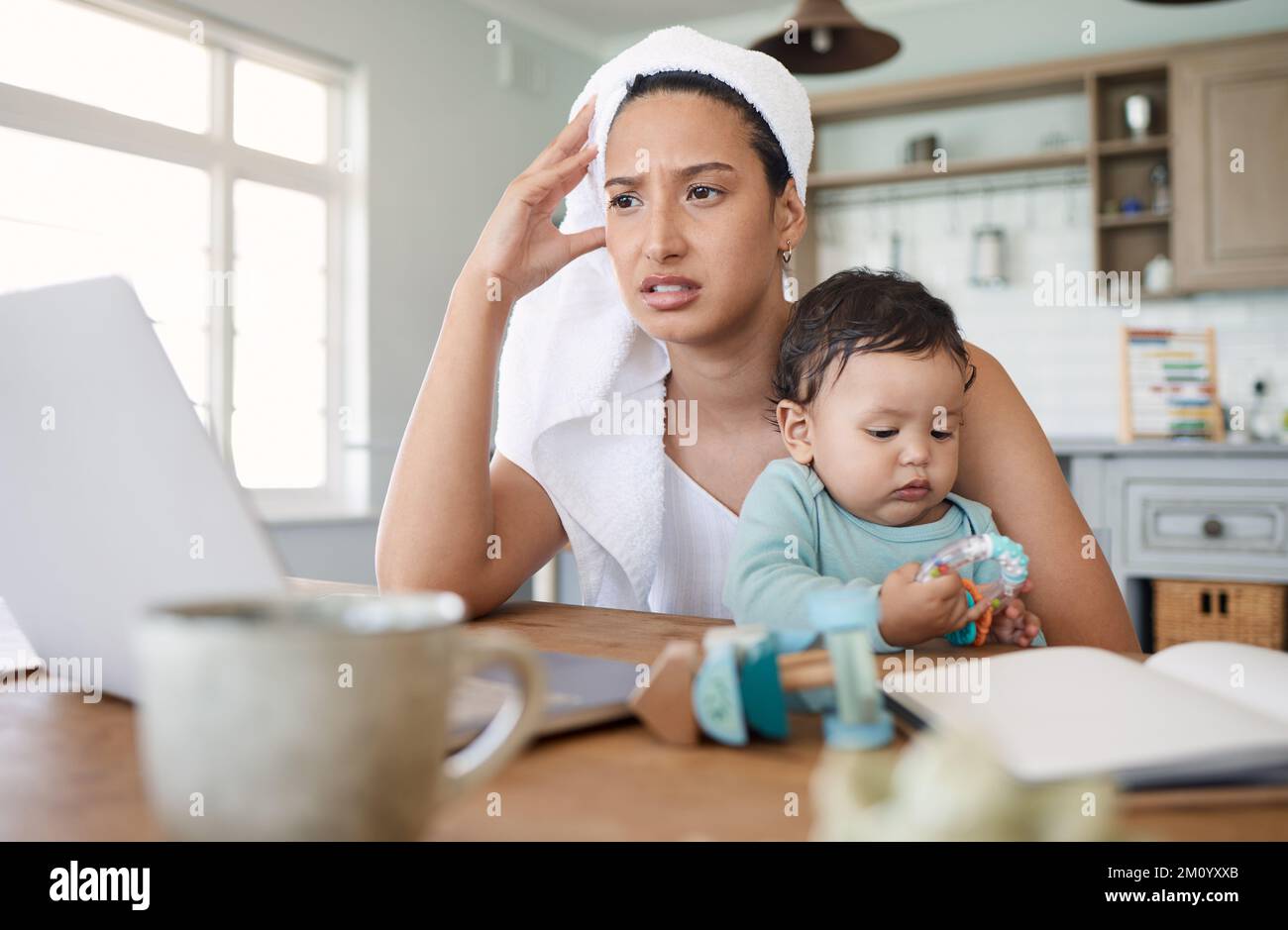 Time flies when you have a busy schedule. a woman looking stressed while looking at her laptop and holding her baby on her lap. Stock Photo