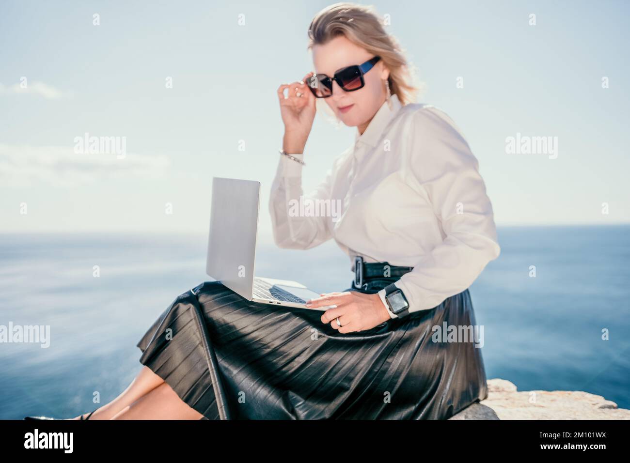 Digital nomad, Business woman working on laptop by the sea. Pretty lady typing on computer by the sea at sunset, makes a business transaction online Stock Photo