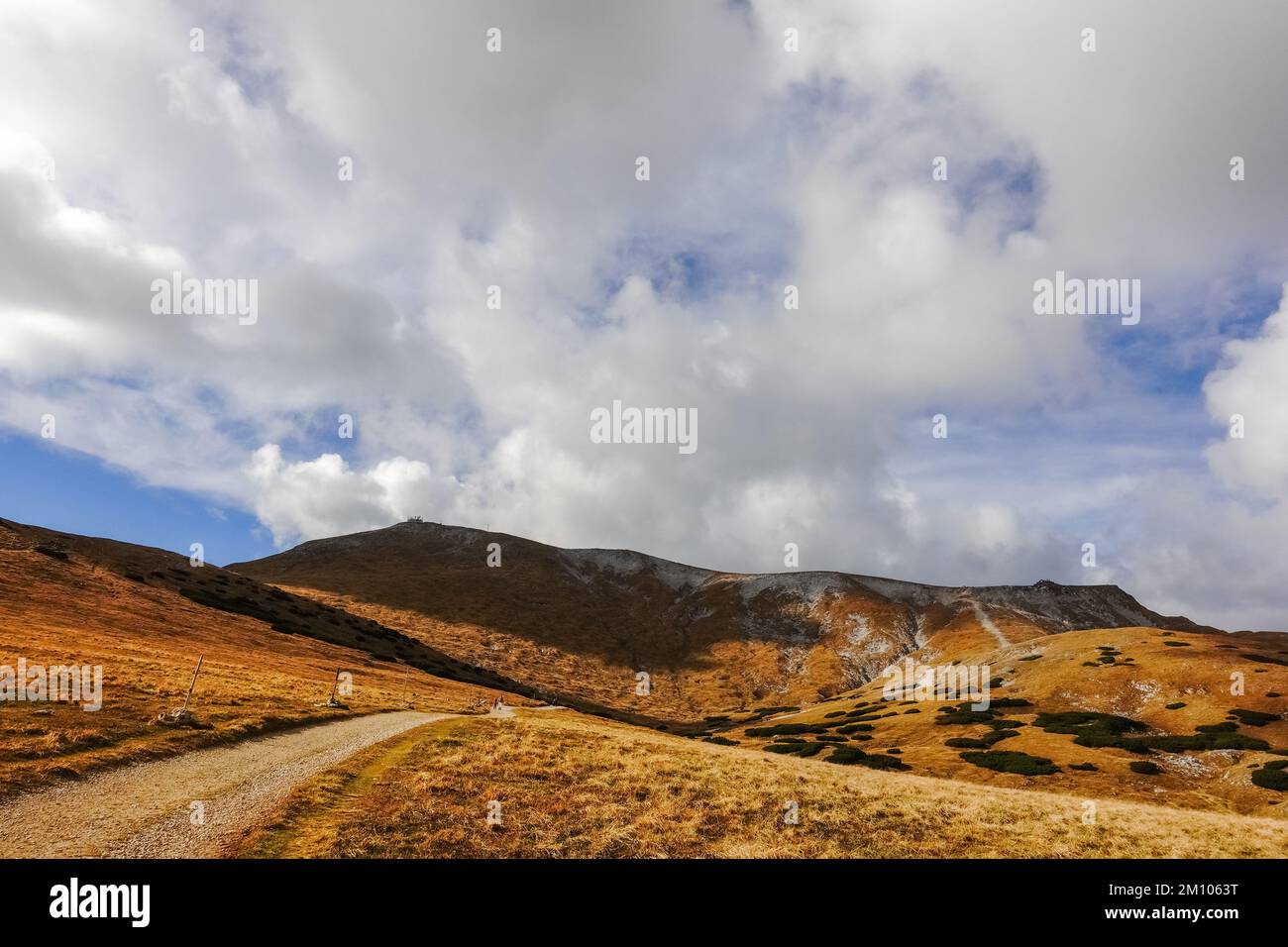long dirt road through a hilly landscape at the top from a mountain in austria Stock Photo