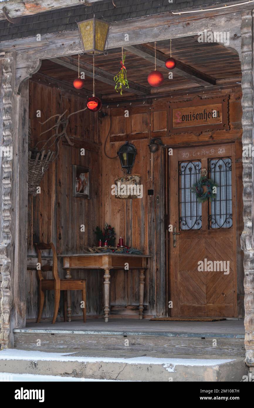 weihnachtlich geschmückter Hauseingang, mit roten Christbaumkugeln, Tisch und Stuhl am Eingang zum Holzhaus. Stock Photo