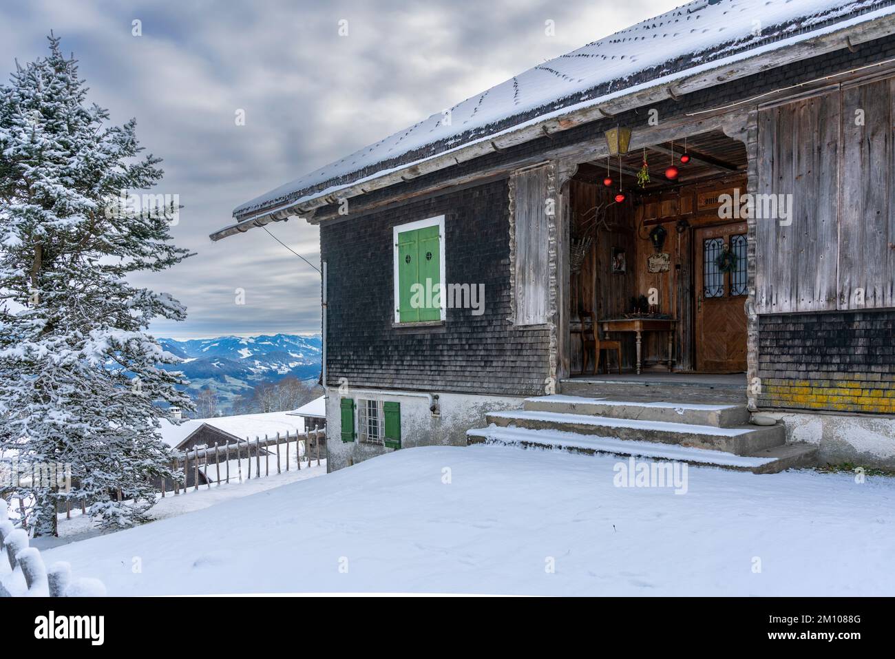 weihnachtlich geschmückter Hauseingang, mit roten Christbaumkugeln, Tisch und Stuhl am Eingang zum Holzhaus. Stock Photo